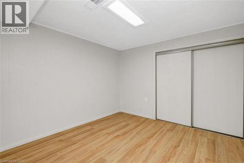 Room featuring wood-finish flooring, light-toned wall paneling, and a dual sliding-door closet with metal frames - 14 Niagara Street, Hamilton, ON 