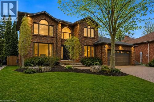 Two-story brick exterior residence featuring a front-facing attached garage, arched window accents, a paved driveway, and mature landscaping - 28 Deerview Avenue, Ancaster, ON 