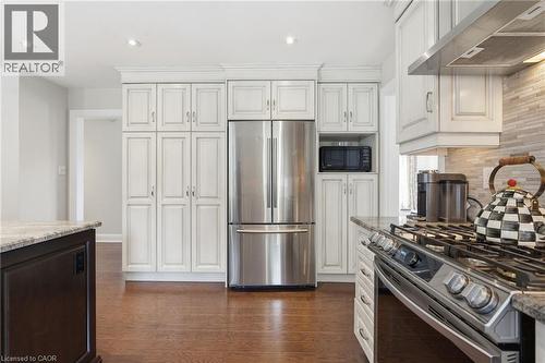 Kitchen featuring stainless steel appliances, light stone countertops, dark wood-style floors, recessed lighting, and backsplash - 28 Deerview Avenue, Ancaster, ON 