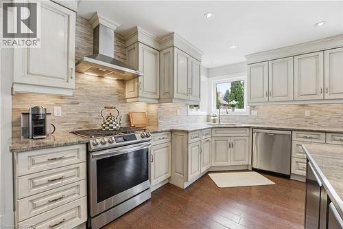Kitchen featuring stainless steel appliances, light stone countertops, dark wood finished floors, recessed lighting, and decorative backsplash - 28 Deerview Avenue, Ancaster, ON 