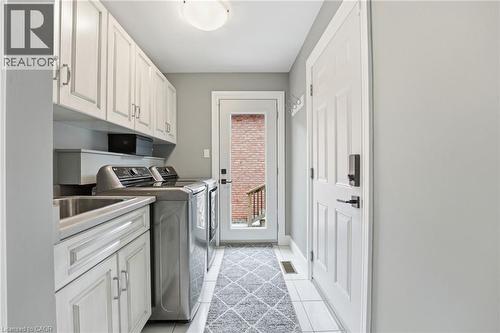 Laundry area with washing machine and dryer, cabinet space, and light tile patterned floors - 28 Deerview Avenue, Ancaster, ON 