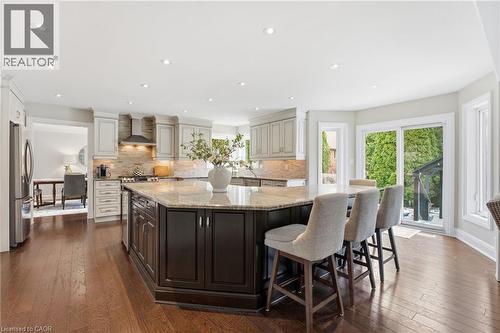 Dual tone kitchen featuring dark wood-style floors, a large island, light stone countertops, dual tone cabinets, and freestanding refrigerator - 28 Deerview Avenue, Ancaster, ON 