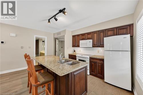 Kitchen with white appliances, light stone countertops, rail lighting, backsplash, and a breakfast bar - 90 Highland Drive Unit# 2014/15, Simcoe, ON 