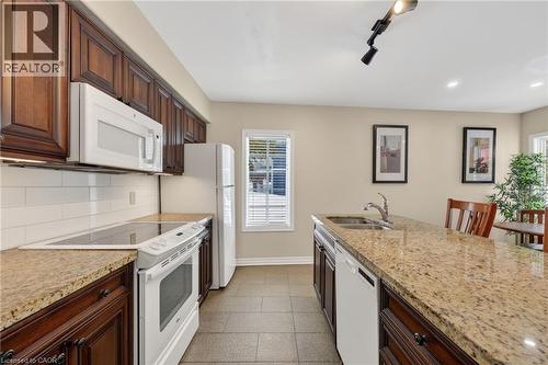 Kitchen featuring white appliances, dark wood finish cabinetry, light stone counters, track lighting, and decorative backsplash - 90 Highland Drive Unit# 2014/15, Simcoe, ON 