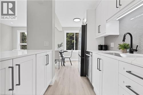 Bright kitchen featuring white shaker cabinetry, quartz countertops, a herringbone tile backsplash, and wood-finish flooring - 71 Blucher Street Unit# G, Kitchener, ON 