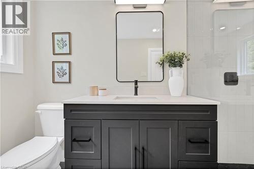 Bathroom featuring a dark wood-finish vanity with a light countertop, a rectangular mirror with a black frame, and a glass-enclosed shower with white tiled walls - 71 Blucher Street Unit# G, Kitchener, ON 