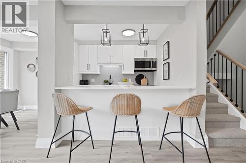 Modern kitchen featuring white cabinetry, stainless steel microwave, black faucet, and chevron tile backsplash - 71 Blucher Street Unit# G, Kitchener, ON 