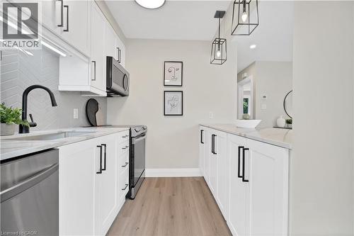 Galley kitchen featuring white shaker cabinetry with black hardware, stainless steel appliances, a chevron-patterned tile backsplash, and wood-finish flooring - 71 Blucher Street Unit# G, Kitchener, ON 