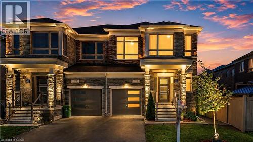 Contemporary semi-detached exterior with a stone and brick facade, multiple large windows, and a black shingle roof. Virtual Twilight - 101 Westfield Crescent, Waterdown, ON 