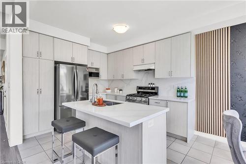 Modern kitchen featuring light wood-finish cabinetry, stainless steel appliances, a center island with a white countertop, and a tiled backsplash - 101 Westfield Crescent, Waterdown, ON 