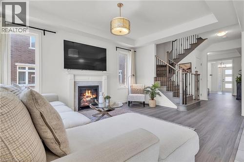 Open-concept living area featuring a built-in fireplace with a white mantel, contemporary chandelier, wood-finish flooring, and a multi-level staircase with dark railings - 101 Westfield Crescent, Waterdown, ON 