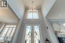 Two-story foyer featuring an ornate chandelier, a transom window, and double entry doors with decorative glass inserts - 