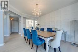 Dining area featuring a prominent chandelier, white paneled accent wall, light wood-finish flooring, crown molding, and an arched entryway - 