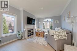 Living area featuring light wood-finish flooring, a contemporary fireplace with a light-toned mantel, crown molding, and recessed lighting - 