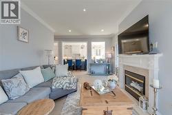 Living room featuring recessed lighting, crown molding, light wood-finish flooring, and a fireplace with a white mantel and stone surround - 