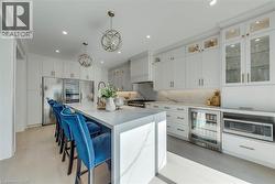 Spacious kitchen featuring an oversized waterfall island with seating, extensive white cabinetry, integrated stainless steel appliances, and matching marble-look countertops and backsplash - 