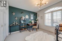 Room featuring an arched window with louvered blinds, a modern ceiling light fixture, a dark accent wall, and light-colored carpeting - 