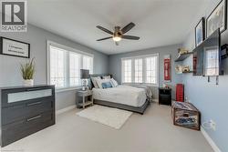 Bedroom featuring light gray walls, two windows with white blinds, and a ceiling fan with integrated lighting - 