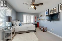 Bedroom featuring multiple windows with blinds, a ceiling fan with integrated lighting, wall-mounted shelving, and light-colored carpeting - 
