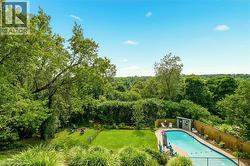 Expansive outdoor space featuring a kidney-shaped swimming pool, a fenced-in yard, a manicured lawn, a detached storage shed, and mature trees - 