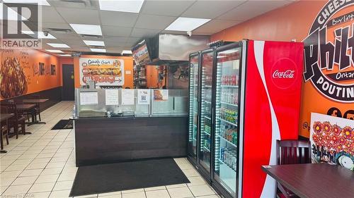 Commercial kitchen space featuring a service counter with a dark wood-finish front, stainless steel overhead exhaust hood, and three glass-front display refrigerators - 2405 Fairview Street, Burlington, ON 