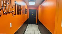 Hallway with two-tone orange and dark brown painted walls, white square floor tiles, and a black door - 