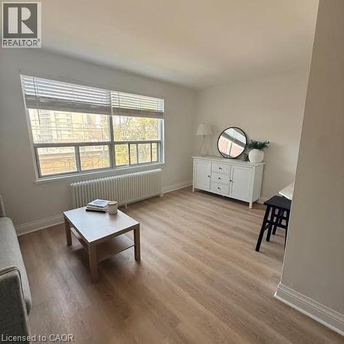 Spacious interior featuring wide-plank wood-finish flooring, a large window with blinds, and white baseboards - 57 Mericourt Road Unit# 111, Hamilton, ON - Indoor Photo Showing Living Room