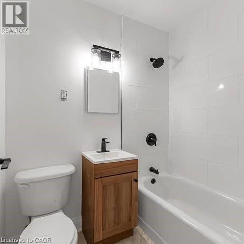 Modern bathroom featuring white subway tile, a white bathtub, and a wood-finish vanity with a white integrated sink - 57 Mericourt Road Unit# 111, Hamilton, ON - Indoor Photo Showing Bathroom