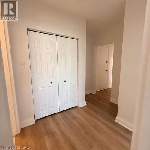 Hallway featuring wood-finish flooring, white baseboards, and a white bi-fold closet with black hardware - 57 Mericourt Road Unit# 111, Hamilton, ON - Indoor