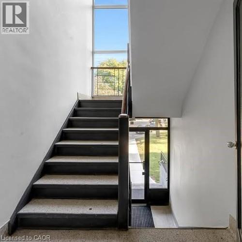 Modern staircase featuring a dark wood handrail, light-colored treads, and a clear glass balustrade - 57 Mericourt Road Unit# 111, Hamilton, ON - Indoor Photo Showing Other Room