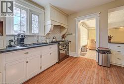 Gourmet kitchen featuring wood-finish flooring, white cabinetry with dark countertops, white subway tile backsplash, a stainless steel range, and a custom range hood - 
