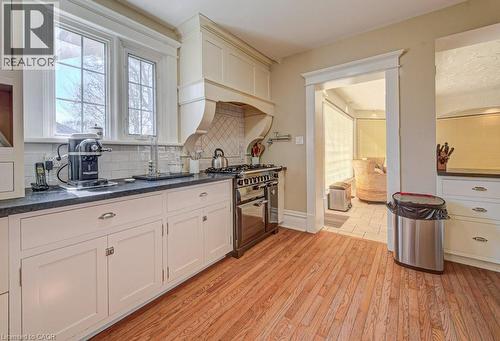 Gourmet kitchen featuring wood-finish flooring, white cabinetry with dark countertops, white subway tile backsplash, a stainless steel range, and a custom range hood - 2032 Coronation Boulevard, Cambridge, ON - Indoor Photo Showing Kitchen