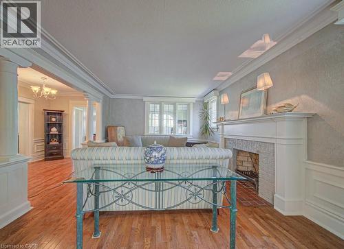 Living area featuring hardwood flooring, extensive crown molding, a white mantel fireplace with brick surround, and wainscoting - 2032 Coronation Boulevard, Cambridge, ON - Indoor With Fireplace