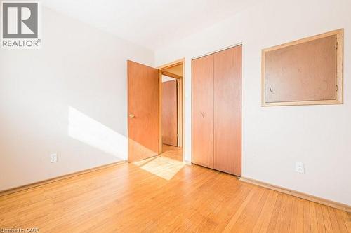 Hardwood-style flooring extends throughout this room, featuring light-toned walls, a natural wood-finish door, and bi-fold closet doors - 66 Summit Avenue, Kitchener, ON - Indoor Photo Showing Other Room