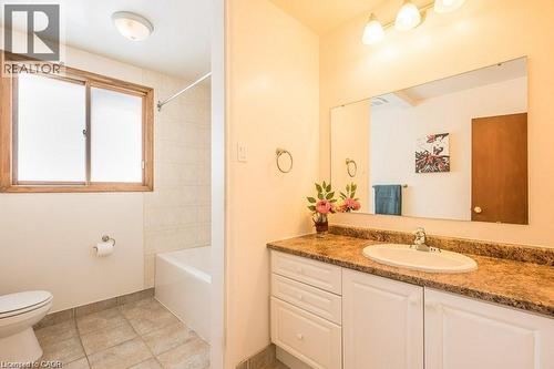 Bathroom featuring a single vanity with an integrated sink, a large mirror, a three-light vanity fixture, a bathtub with tile surround, and a frosted glass window with a wood frame - 66 Summit Avenue, Kitchener, ON - Indoor Photo Showing Bathroom