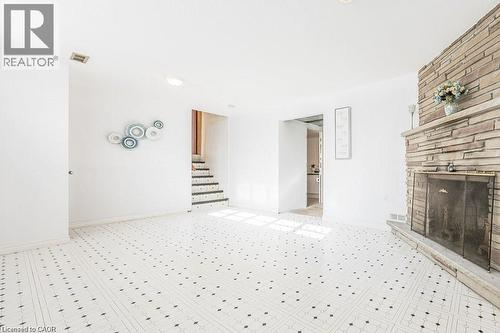 Spacious room featuring patterned flooring, a stone-faced fireplace with a metal screen, white painted walls, and a staircase with dark risers - 66 Summit Avenue, Kitchener, ON - 