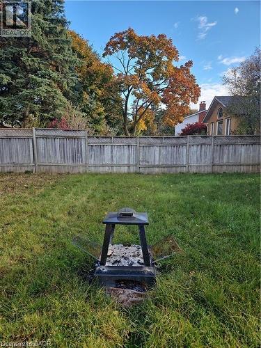 Expansive grassy yard featuring a wood privacy fence, mature trees, and a built-in fire pit - 66 Summit Avenue, Kitchener, ON - Outdoor With Backyard