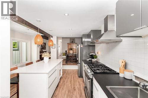 Modern kitchen featuring a large center island with integrated storage, stainless steel appliances, a gas range with a coordinating vent hood, and wood-finish flooring - 134 Erie Avenue, Hamilton, ON 