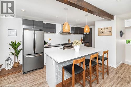 Modern kitchen featuring a white quartz island countertop, stainless steel appliances, white subway tile backsplash, dark flat-panel cabinetry, and wood-finish flooring - 134 Erie Avenue, Hamilton, ON 
