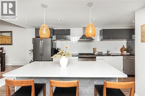 Spacious kitchen featuring a large island with a light-toned countertop, stainless steel appliances, dark flat-panel cabinetry, white subway tile backsplash, and recessed lighting - 134 Erie Avenue, Hamilton, ON 