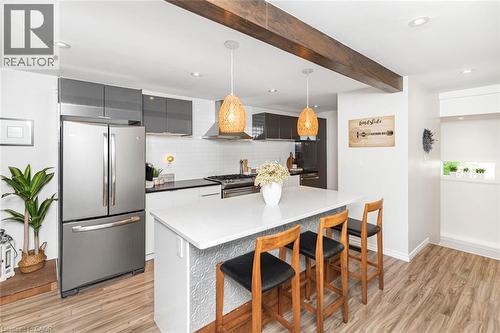 Modern kitchen featuring a white center island with seating, pendant lighting, stainless steel appliances, and wood-finish flooring - 134 Erie Avenue, Hamilton, ON 