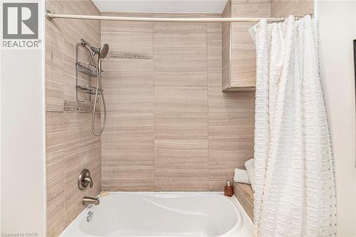 Bathtub with a handheld showerhead, brushed nickel fixtures, and light-toned horizontal tile surround - 134 Erie Avenue, Hamilton, ON 
