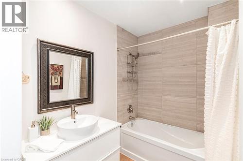 Bathroom featuring a white vanity with a vessel sink, a framed mirror, a bathtub with shower head, and tile-surround shower walls - 134 Erie Avenue, Hamilton, ON 