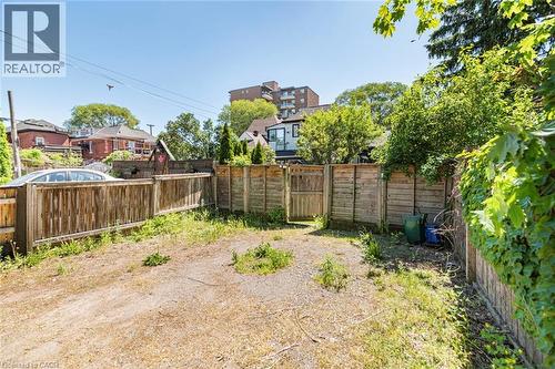 Fenced property with a large open area, mature perimeter foliage, and a wooden gate - 134 Erie Avenue, Hamilton, ON 