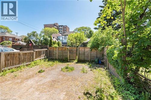 Spacious outdoor area featuring a wooden privacy fence, mature perimeter trees, and a clear sky backdrop - 134 Erie Avenue, Hamilton, ON 