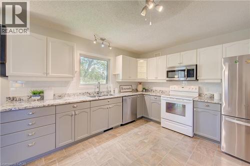 Kitchen with two-tone cabinetry, stainless steel appliances, granite-style countertops, and a subway tile backsplash - 137 Wesley Crescent, Waterloo, ON 