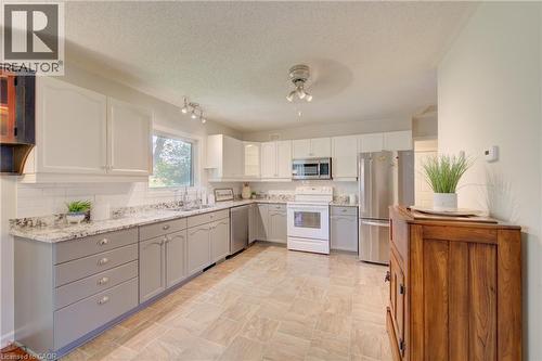 Kitchen featuring two-tone cabinetry with white upper and gray lower cabinets, light-toned tile flooring, subway tile backsplash, stainless steel appliances, and a window above the sink - 137 Wesley Crescent, Waterloo, ON 