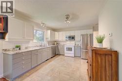 Kitchen featuring two-tone cabinetry with white upper and gray lower cabinets, light-toned tile flooring, subway tile backsplash, stainless steel appliances, and a window above the sink - 