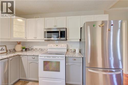 Kitchen featuring two-tone cabinetry with upper white cabinets and lower gray cabinets, speckled countertops, a white subway tile backsplash, and stainless steel appliances including an over-the-range - 137 Wesley Crescent, Waterloo, ON 
