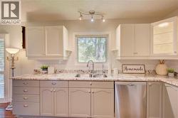 Kitchen featuring white upper cabinetry, grey lower cabinetry, granite countertops, a stainless steel double basin sink with a gooseneck faucet, and a stainless steel dishwasher - 